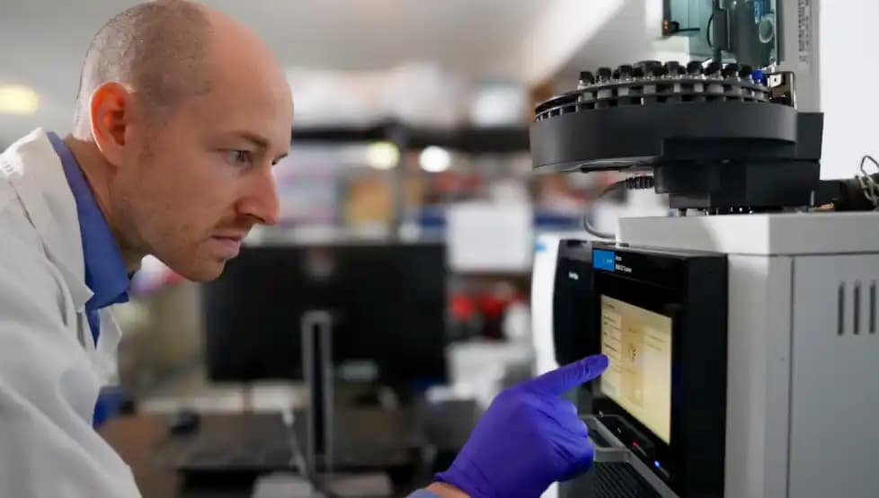 Scientist in a laboratory using an analytical testing machine while wearing gloves.